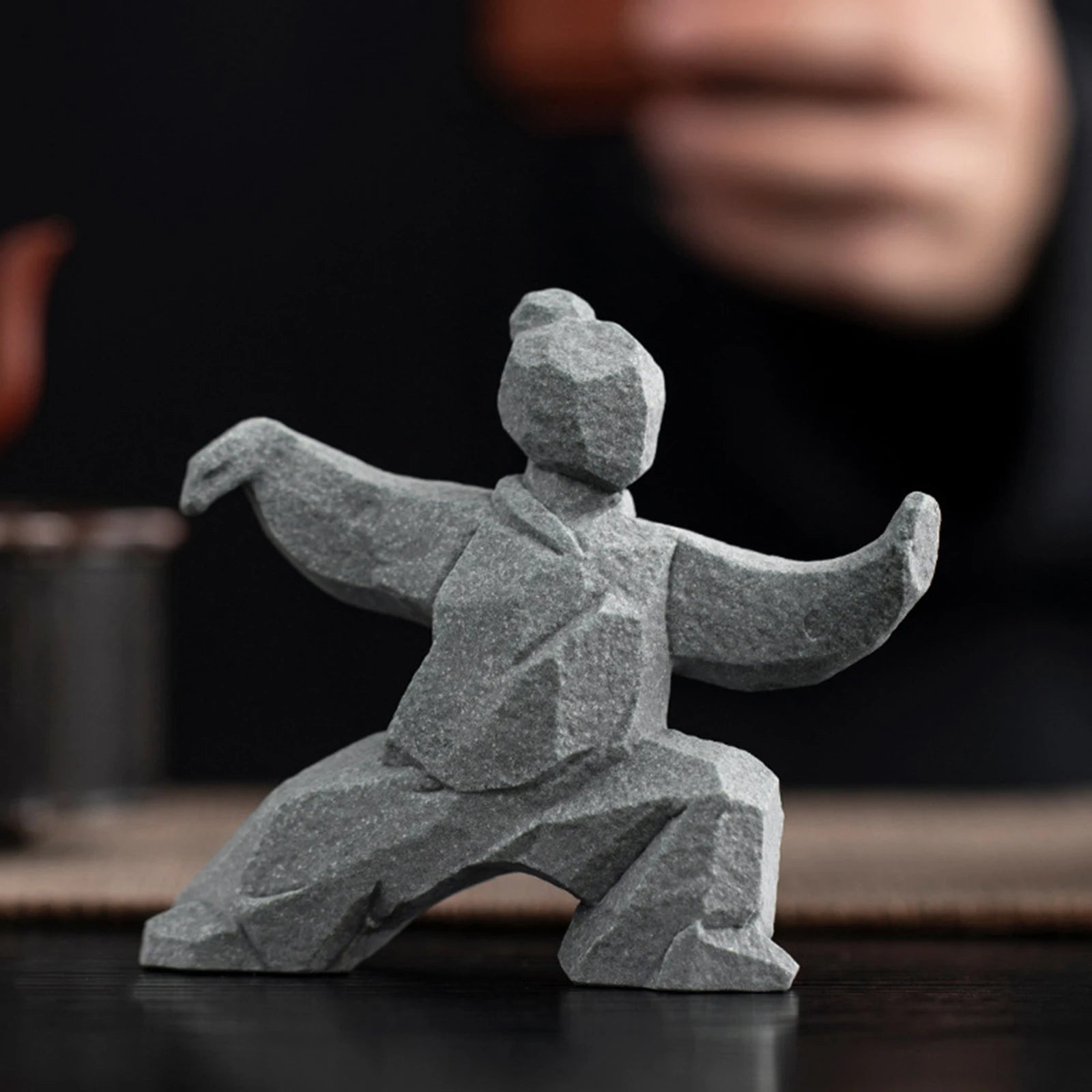 Gray stone sculpture of a martial artist in a dynamic pose on a dark surface.