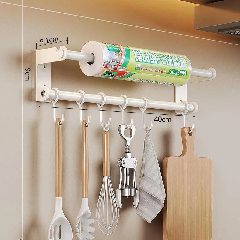 Wall-mounted kitchen organizer with hooks holding utensils, a cutting board, and a roll of paper towels.