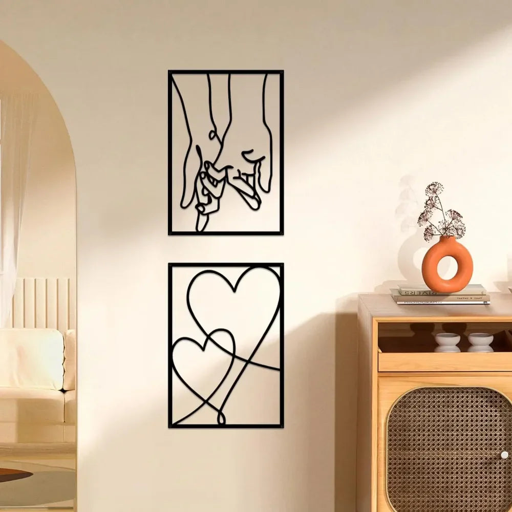 Two black metal wall art pieces on a beige wall with a wooden cabinet and decorative items.