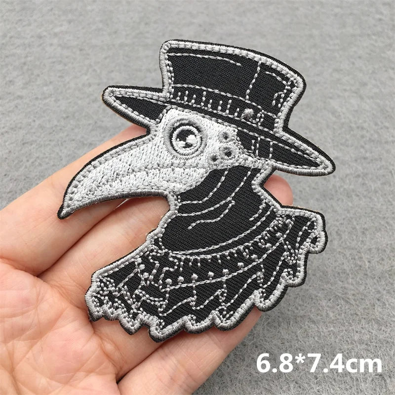 Embroidered patch of a bird wearing a top hat held on a hand with a gray background.