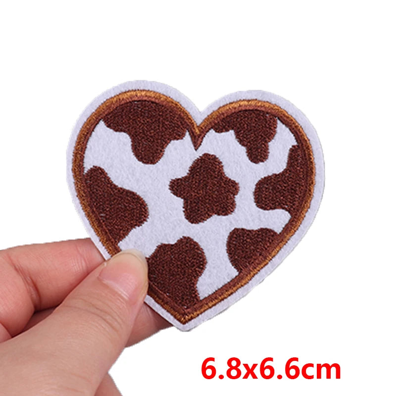 Heart-shaped patch with cow print held by a hand on a white background