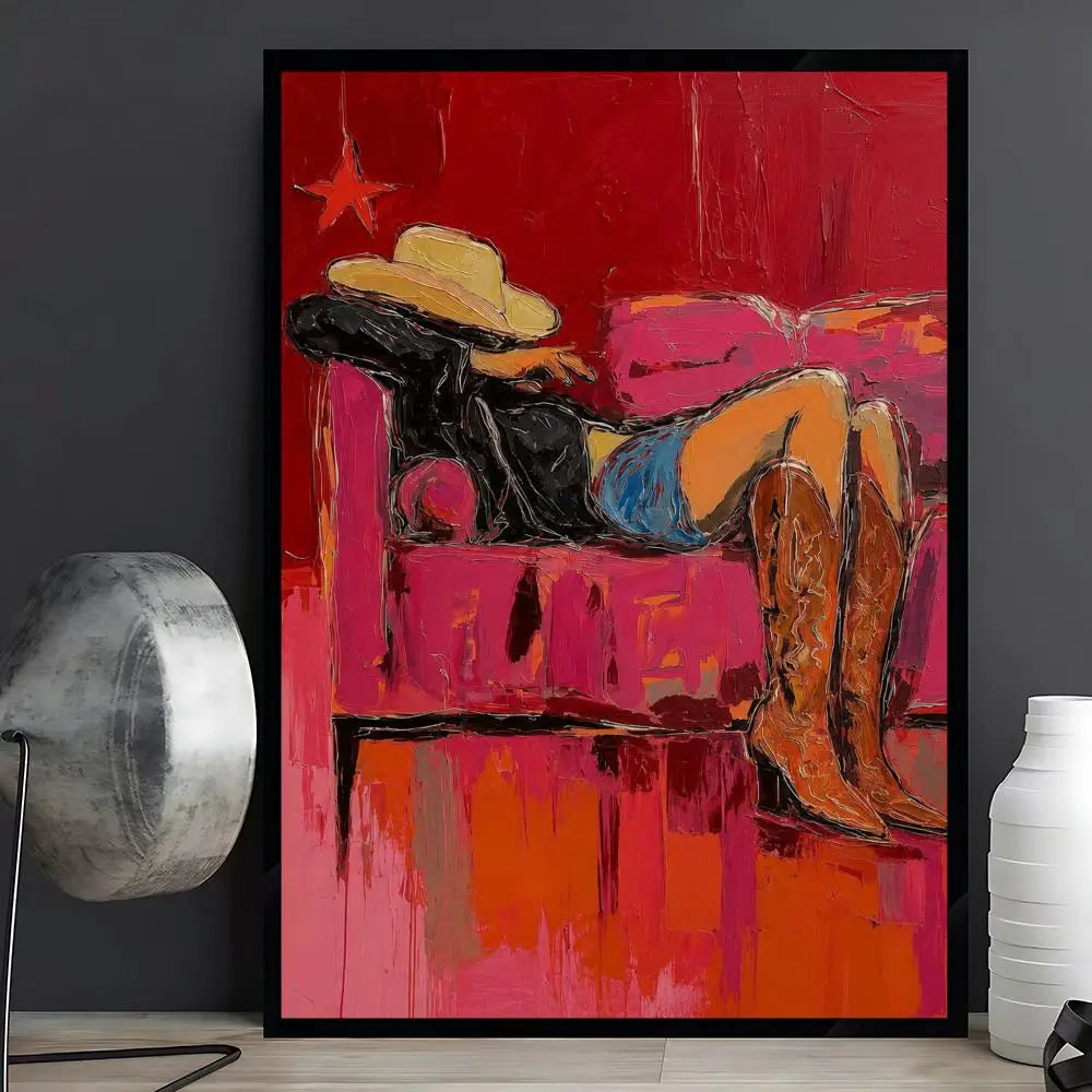 A framed abstract painting featuring a reclining figure in a cowboy hat and boots against a vivid red and pink background, displayed on a tabletop between a metallic lamp and a white vase.