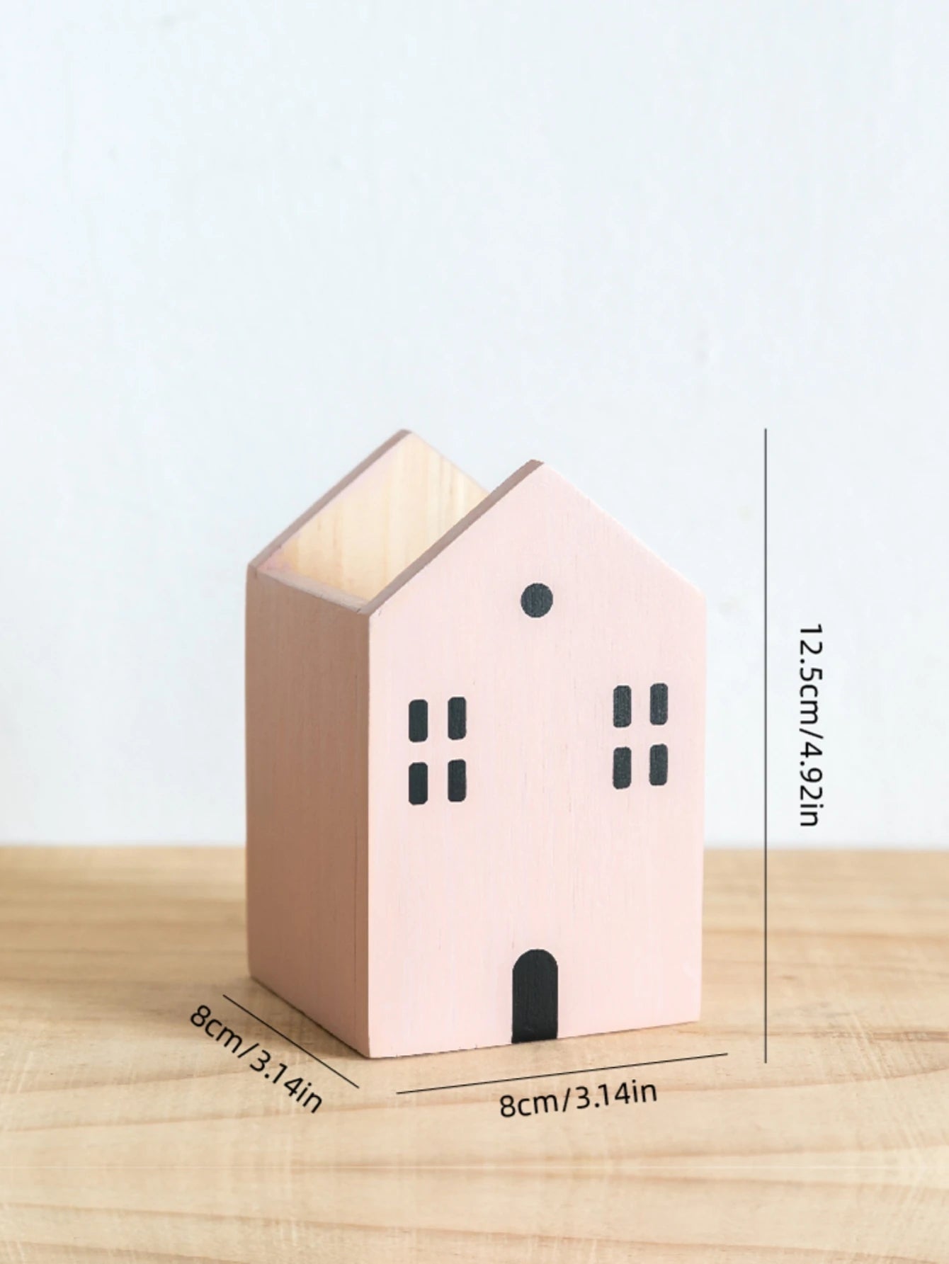 Pink house-shaped candle holder with measurements on a wooden surface
