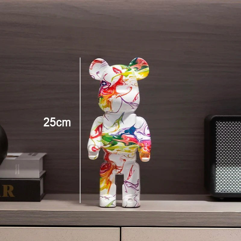 A white bear-shaped collectible figure with colorful paint-splatter artwork stands on a shelf in front of a dark wood wall. A vertical measurement line and the text '25cm' indicate height.