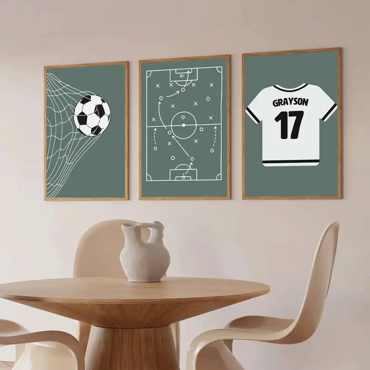 Three framed sports-themed wall art prints hang above a wooden dining table with chairs. The left print shows a soccer ball net, the center shows a football tactic diagram, and the right shows a white soccer jersey with the name Grayson and number 17.