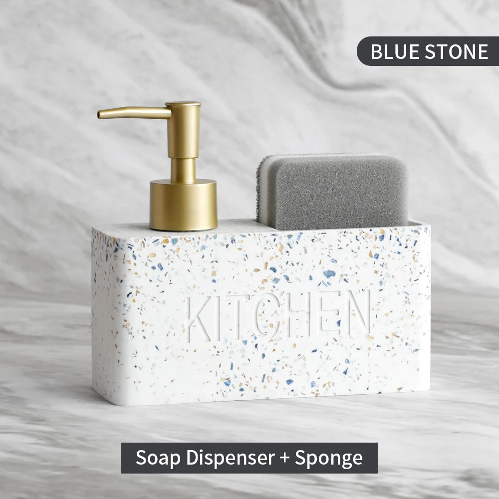 Soap dispenser with gold pump and sponge on a speckled stone block labeled 'Kitchen' against a marble background.