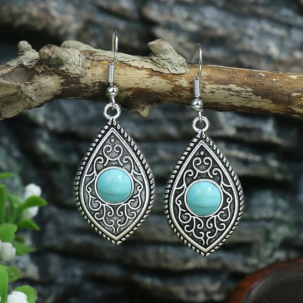 Teardrop-shaped earrings with turquoise stones and silver detailing on a branch.