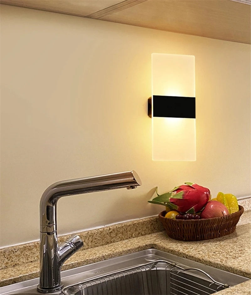 Modern kitchen faucet and sink with a wall-mounted light fixture on a beige wall.