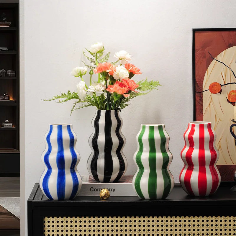 Four colorful striped vases on a shelf with a vase of flowers.