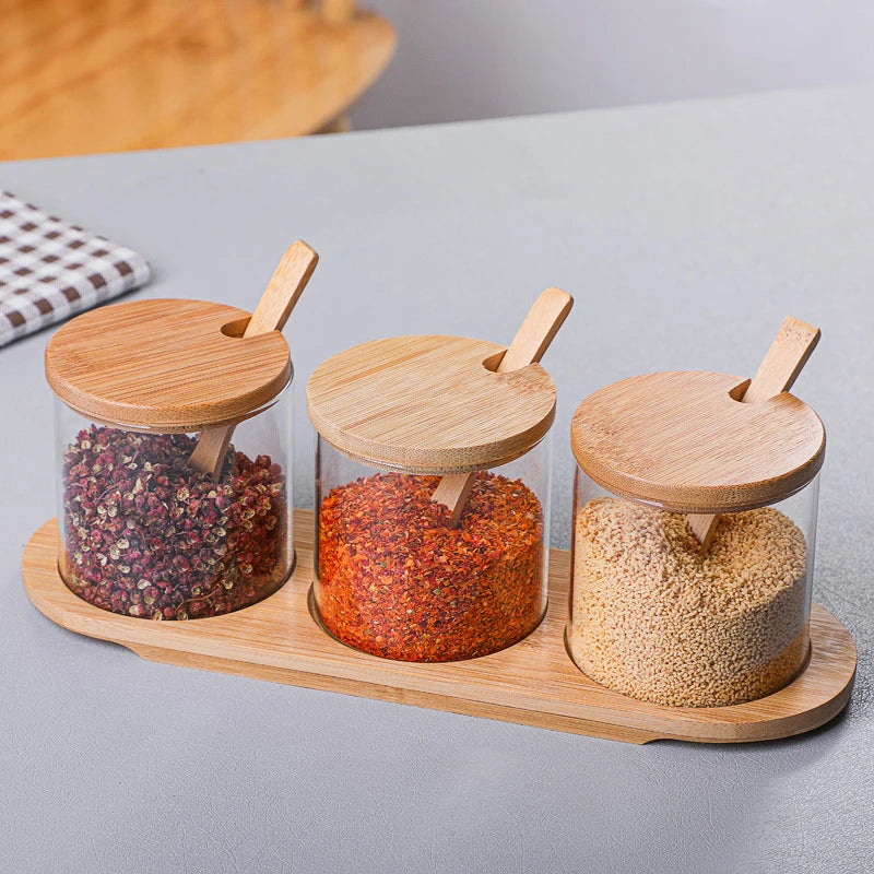 Three glass jars with wooden lids and handles on a wooden tray, containing different spices.