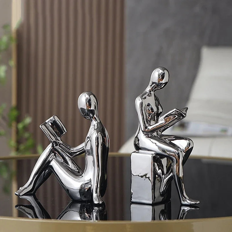 Two chrome bookends shaped like sitting figures on a reflective surface.