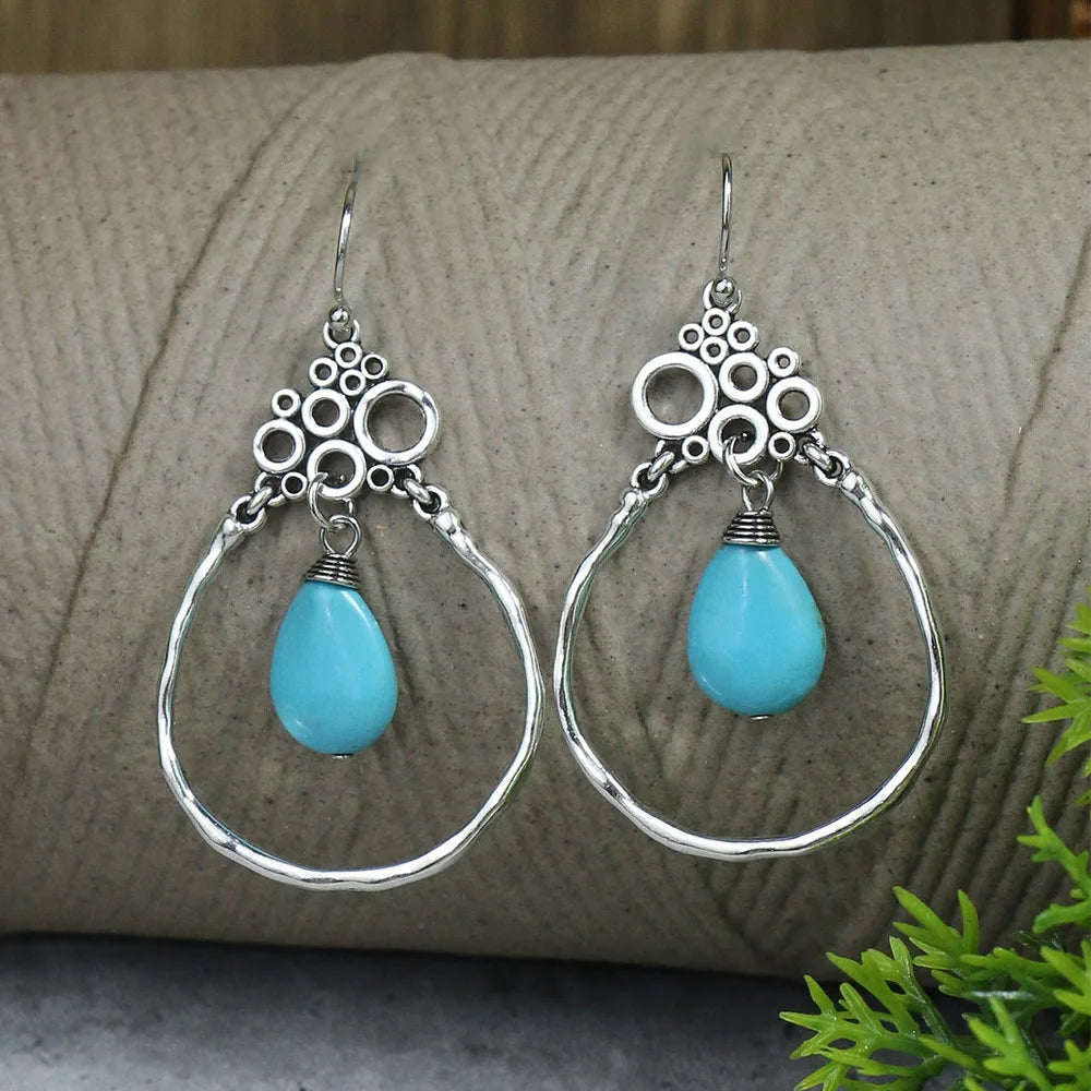 Silver earrings with turquoise teardrop stones on a textured surface.