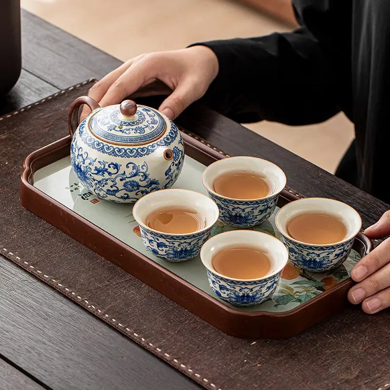 Tea set with blue floral patterns on a wooden tray, held by a person.