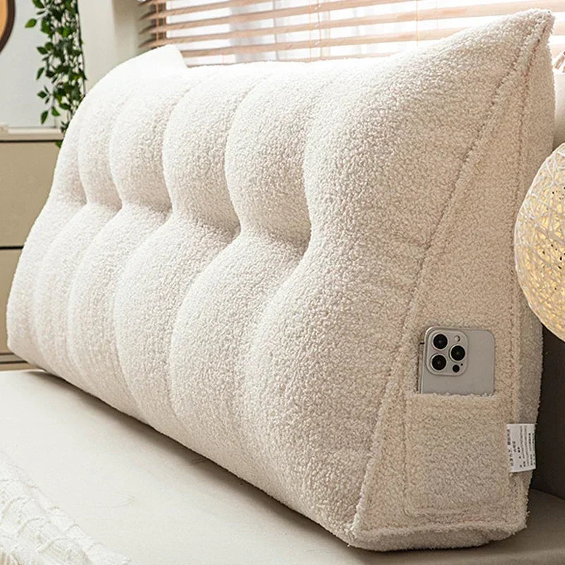 Beige wedge-shaped pillow on a couch with a phone attached to it.