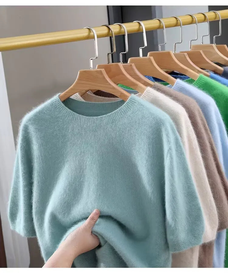 Light blue sweater held by a hand with hangers displaying various colors of sweaters on a rack.