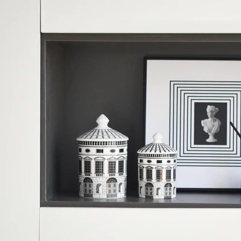 Two black and white ceramic jars on a shelf with a framed picture in the background.