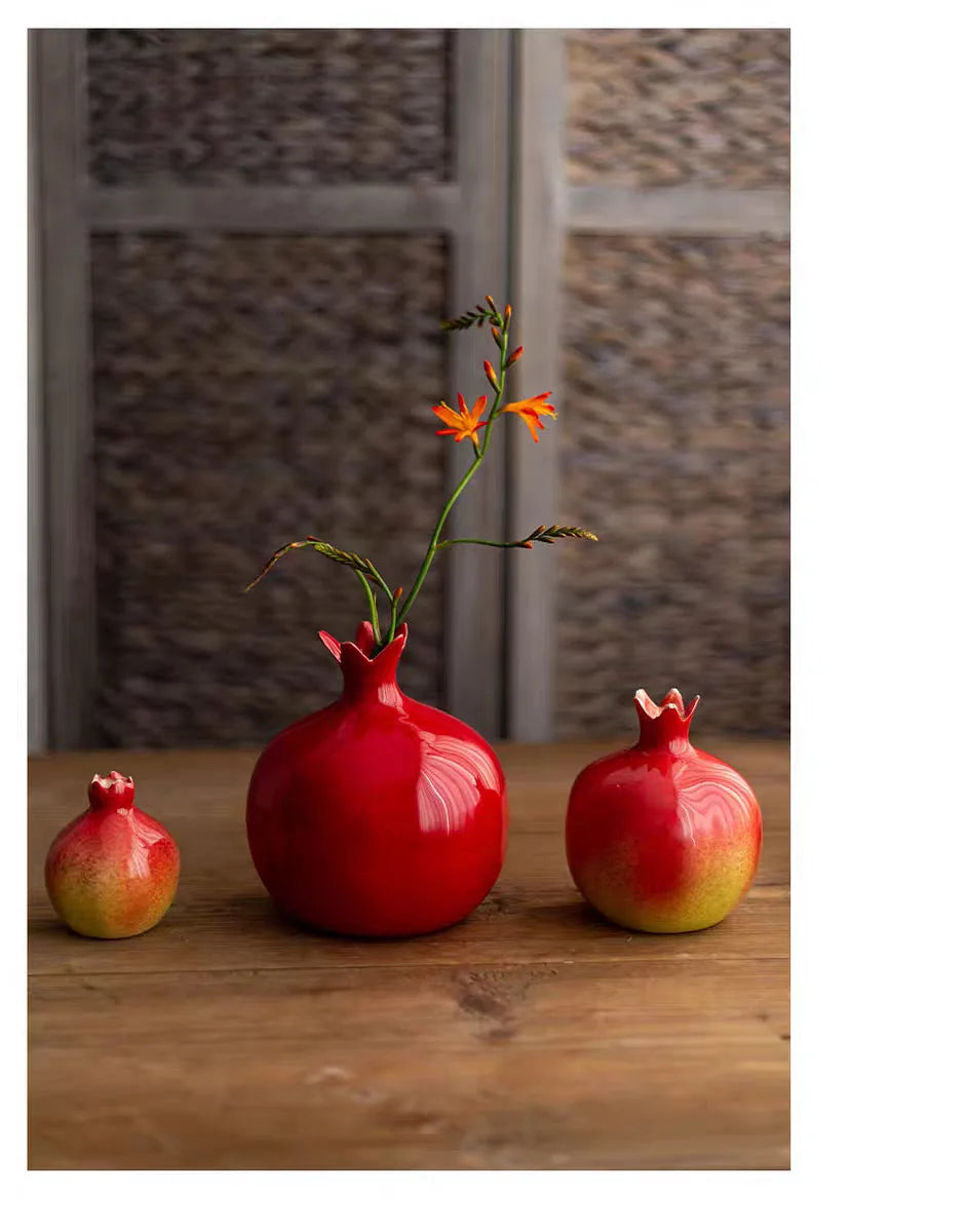 Red ceramic vase with a flower and two pomegranates on a wooden surface.