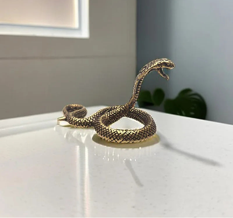 Bronze snake sculpture on a white surface with a neutral background