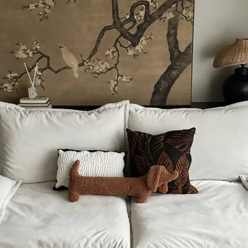 White sofa with a dachshund-shaped cushion against a wall with floral artwork