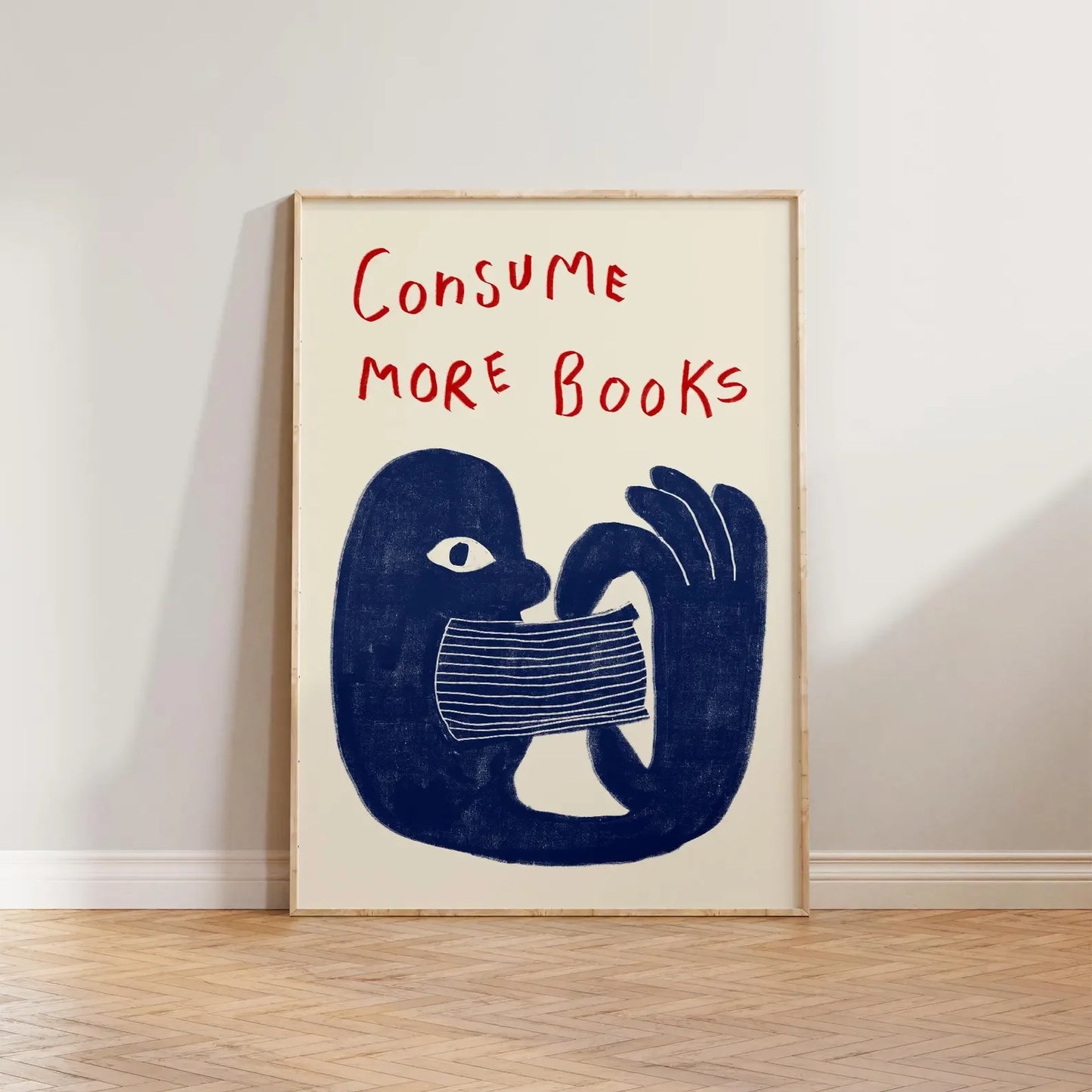 Framed artwork with a blue abstract figure holding a book and text 'CONSUME MORE BOOKS' on a white wall.