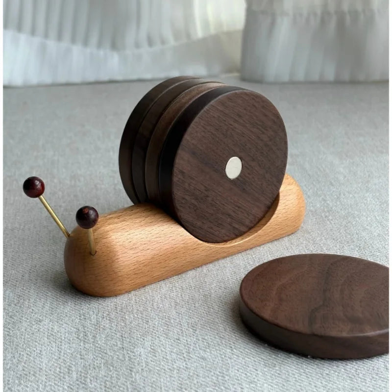 Wooden snail-shaped coaster holder with round wooden coasters forming its shell and two antennae topped with dark wooden beads omn a light grey floor