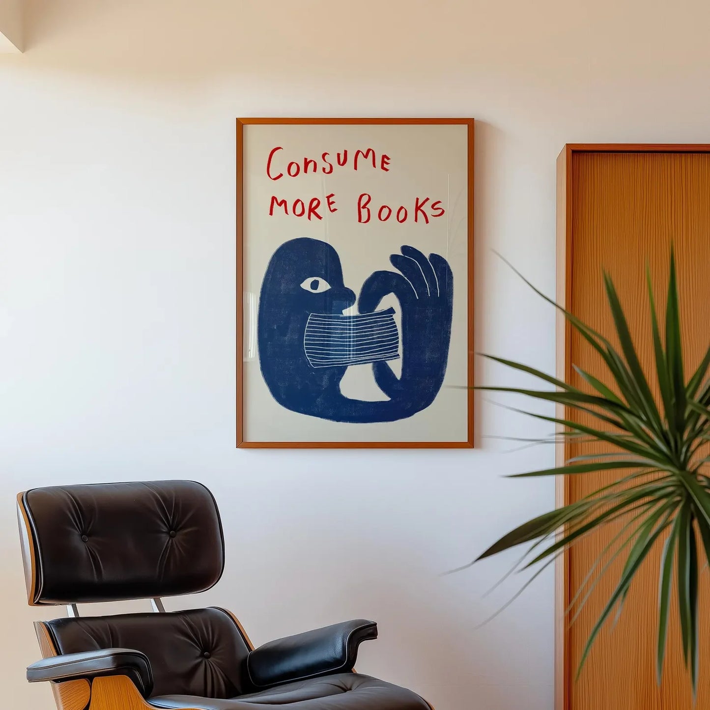 Framed artwork with a blue rooster illustration and 'Consume More Books' text above a brown chair.