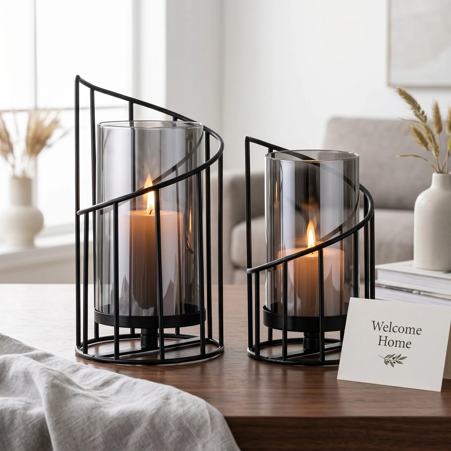 Set of two modern black spiral glass candle holders with smoked hurricane glass displayed on a wooden table in a contemporary home interior.