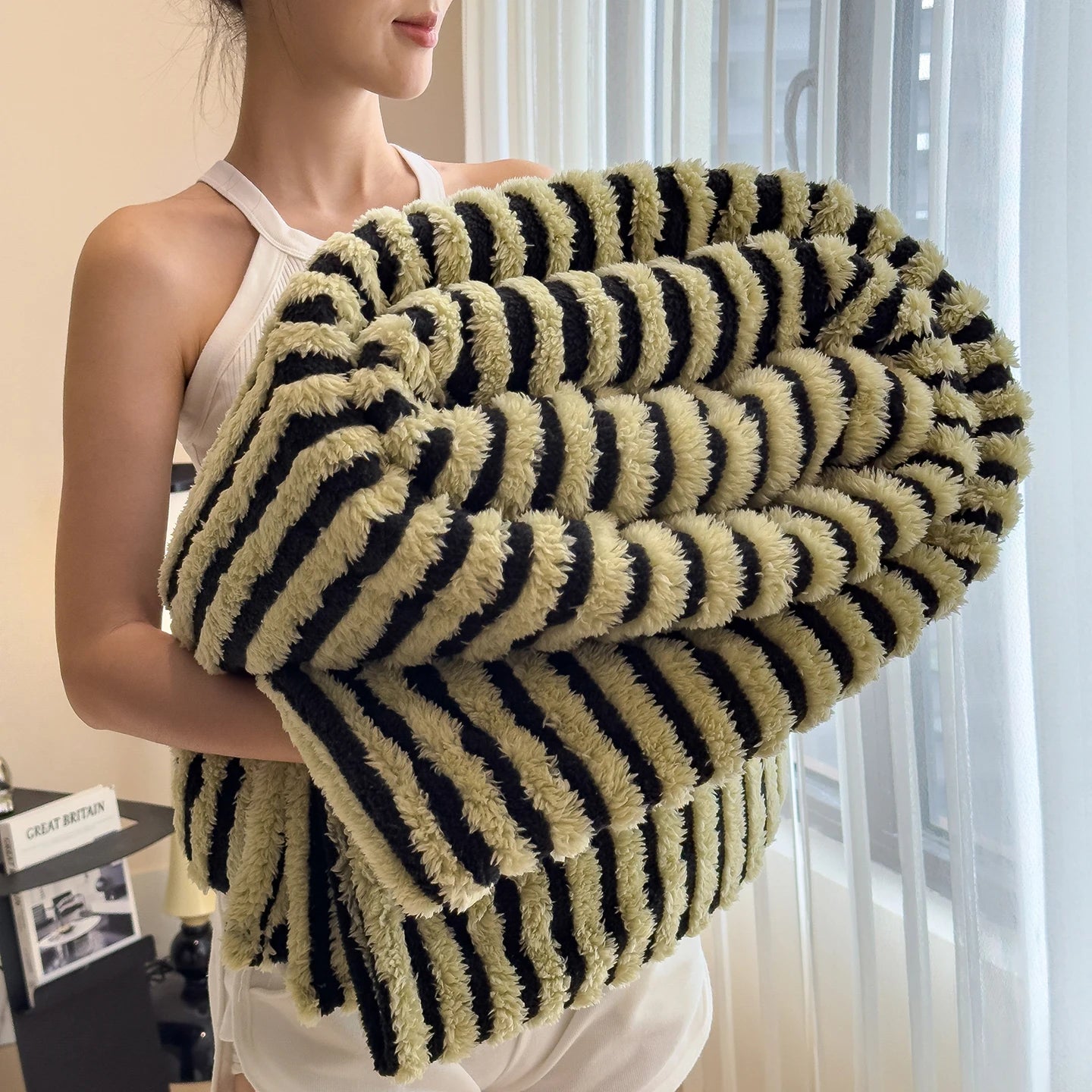 Person holding a striped blanket in a room with light-colored walls and a window.