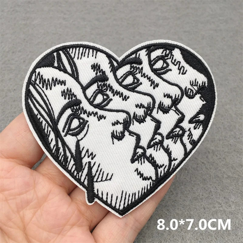 Heart-shaped patch with black and white design held by a hand on a gray background