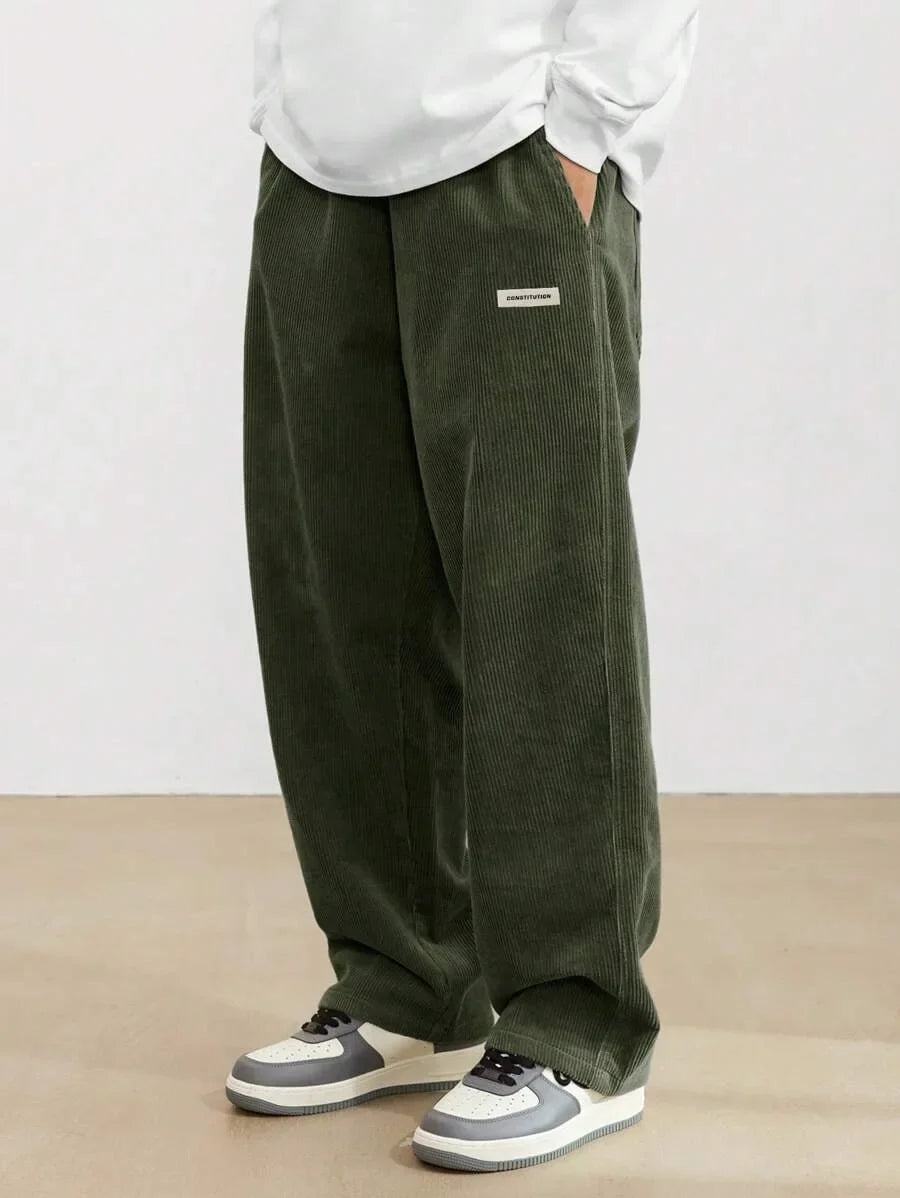 Person wearing green corduroy pants and white sneakers on a plain background