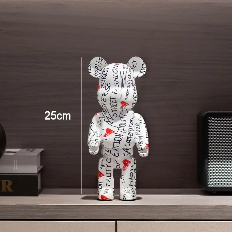 A white bear-shaped collectible figure covered in black graffiti-style text and red heart graphics, standing on a shelf against a dark wood background. A vertical measurement line and the text '25cm' indicate height.