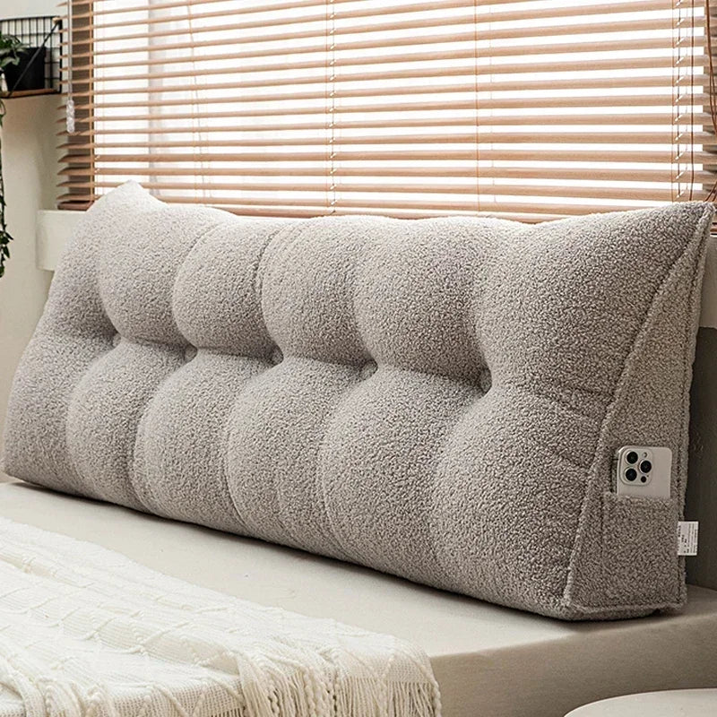 Gray tufted wedge pillow on a bed with a window in the background