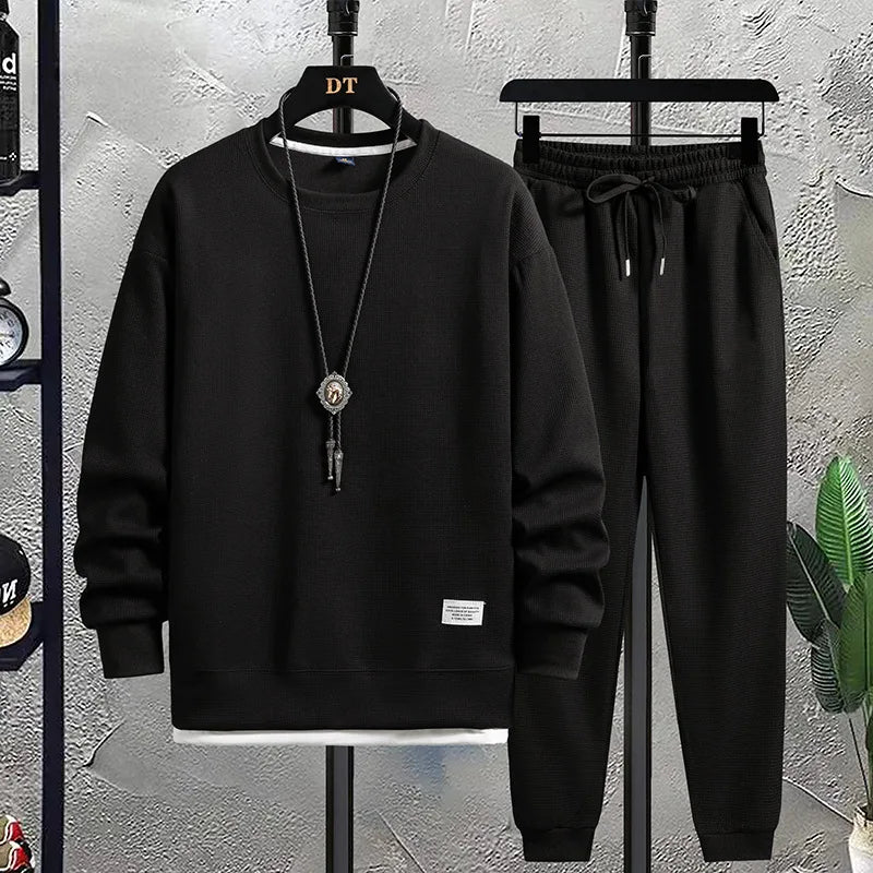 Black sweatshirt and pants set on hangers against a textured wall.