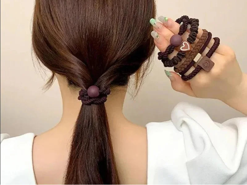 Person with a ponytail wearing hair ties, holding additional hair ties against a neutral background.