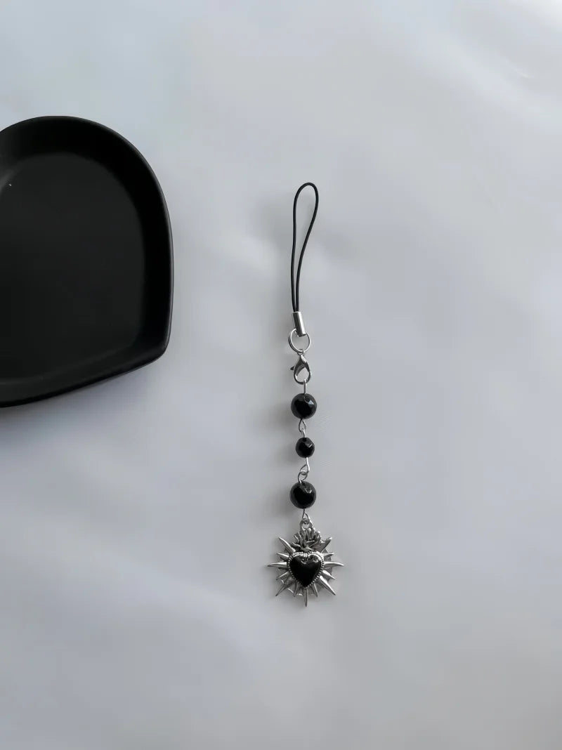 Phone charm with sun design and black heart on a white background