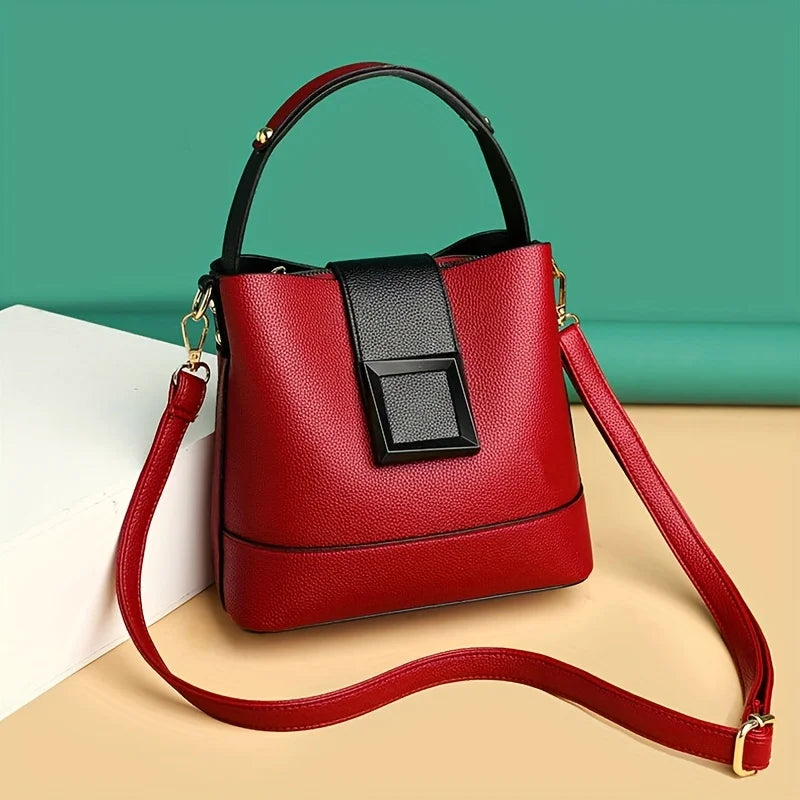 Red handbag with a black accent on a beige surface with a teal background
