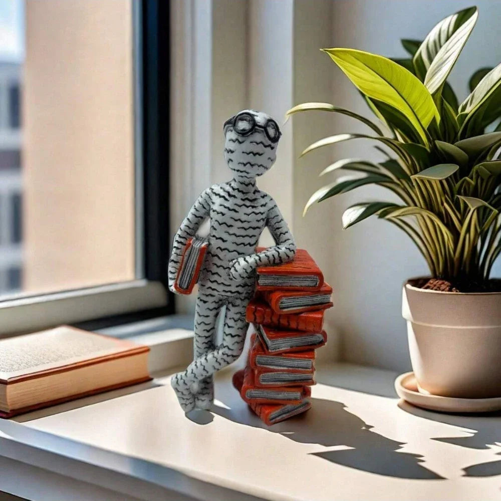Resin reader statue leaning against a stack of books displayed on a windowsill in a modern home.