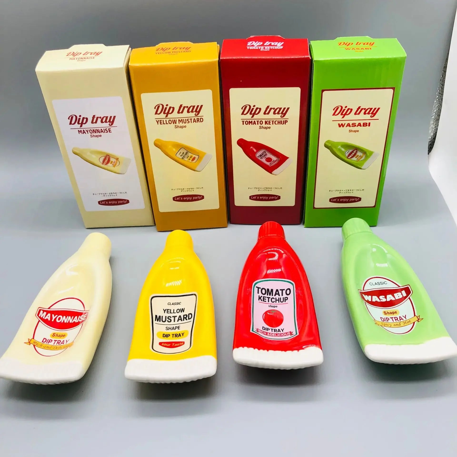 Four miniature plastic dip tray bottles and their corresponding retail boxes arranged on a light gray surface. The bottles and boxes represent mayonnaise, yellow mustard, tomato ketchup, and wasabi flavors.