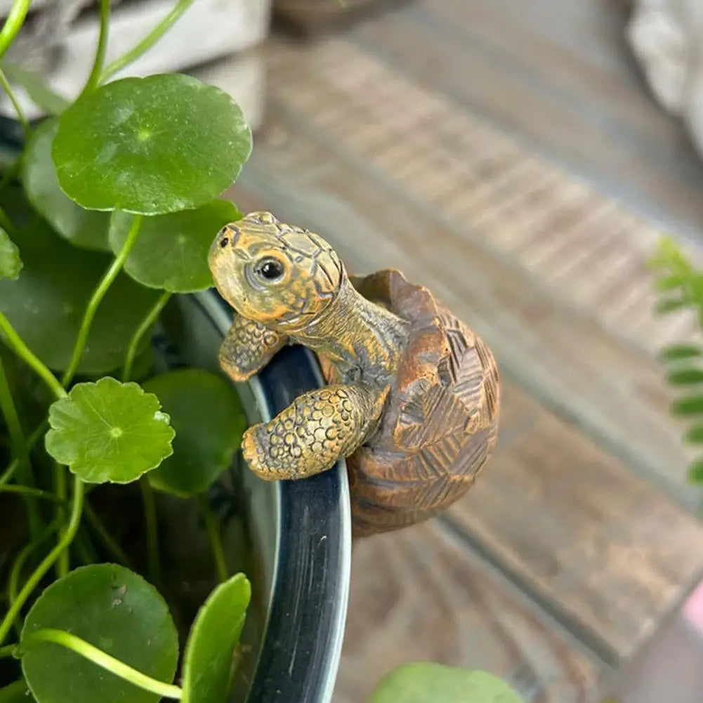 Small turtle figurine on a pot with green leaves in the background