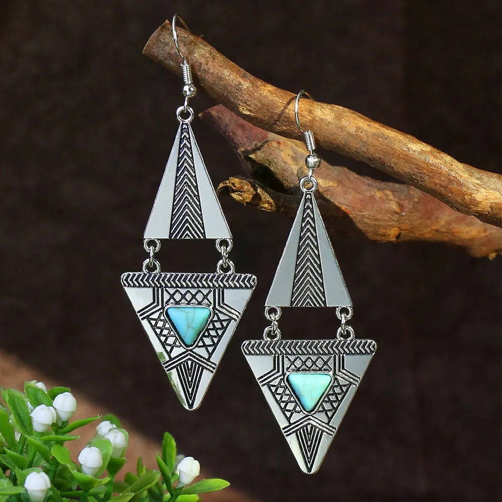 Pair of silver triangle earrings with turquoise stones on a wooden branch.
