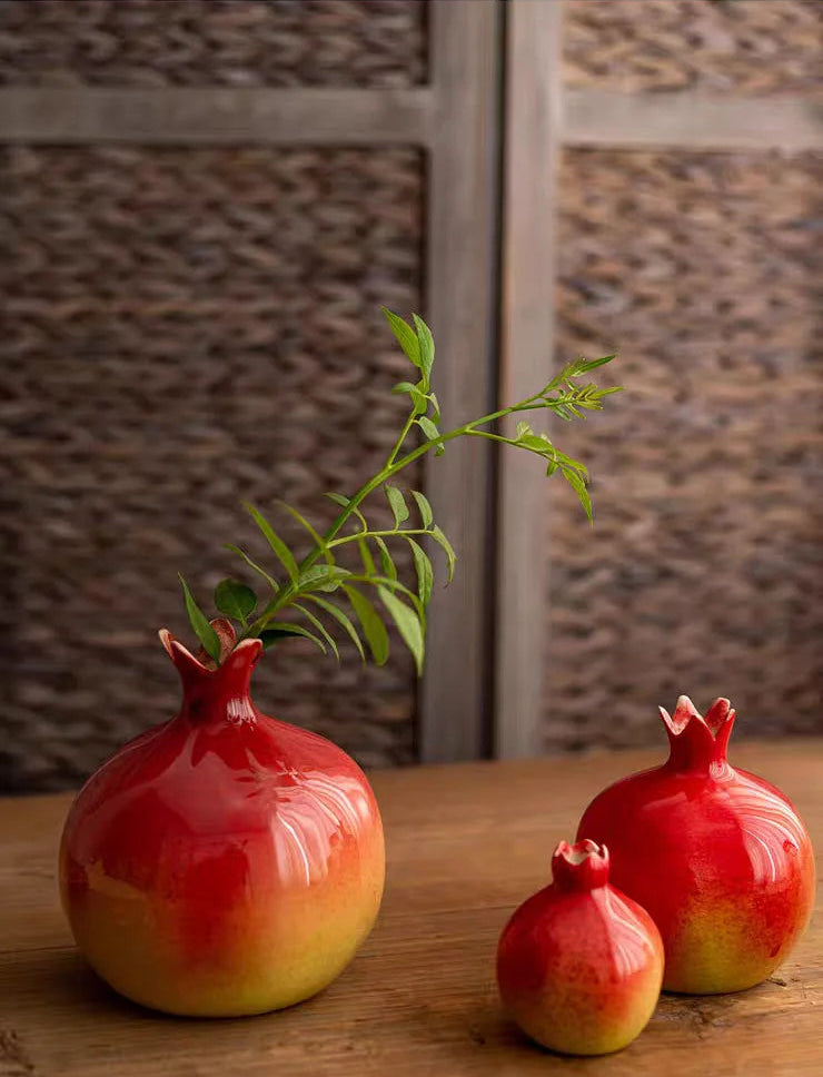 Three red ceramic pomegranate-shaped vases on a wooden surface with a blurred background.