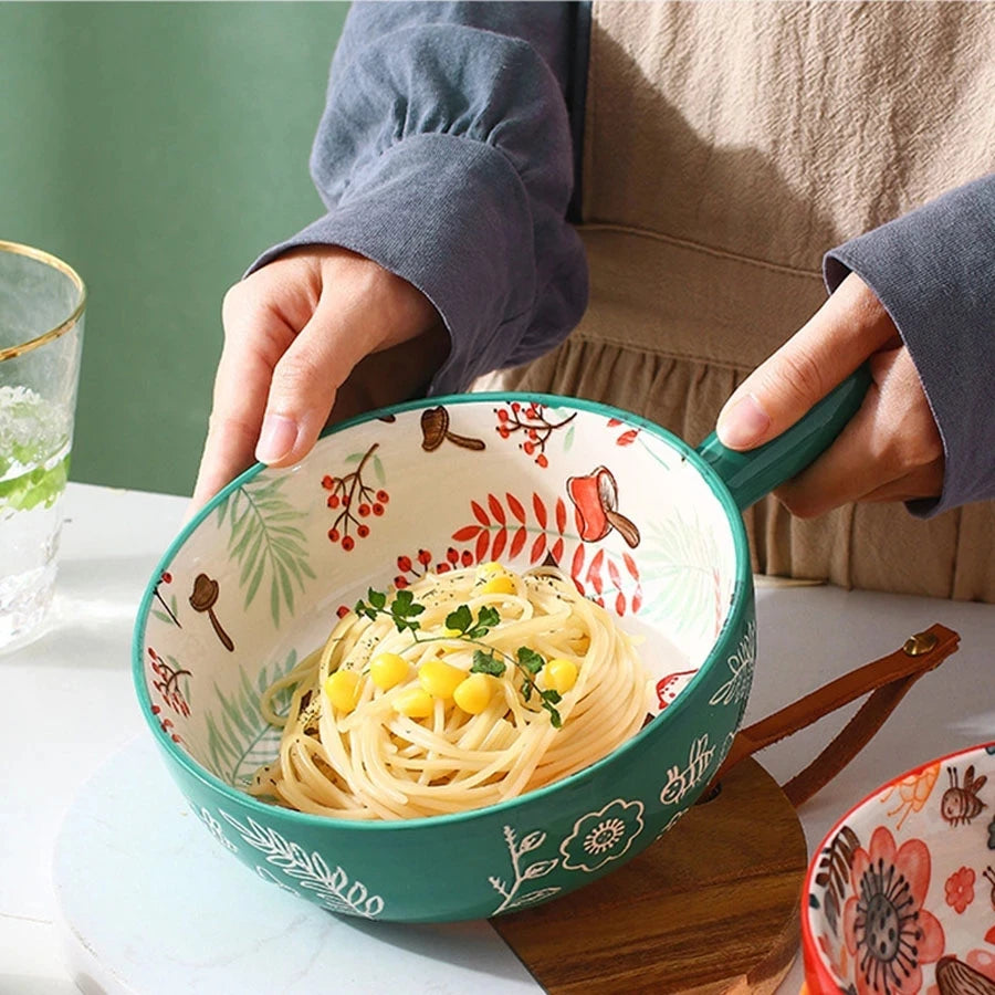 Person holding a decorative bowl with spaghetti, surrounded by a glass of water and a wooden spoon on a table.