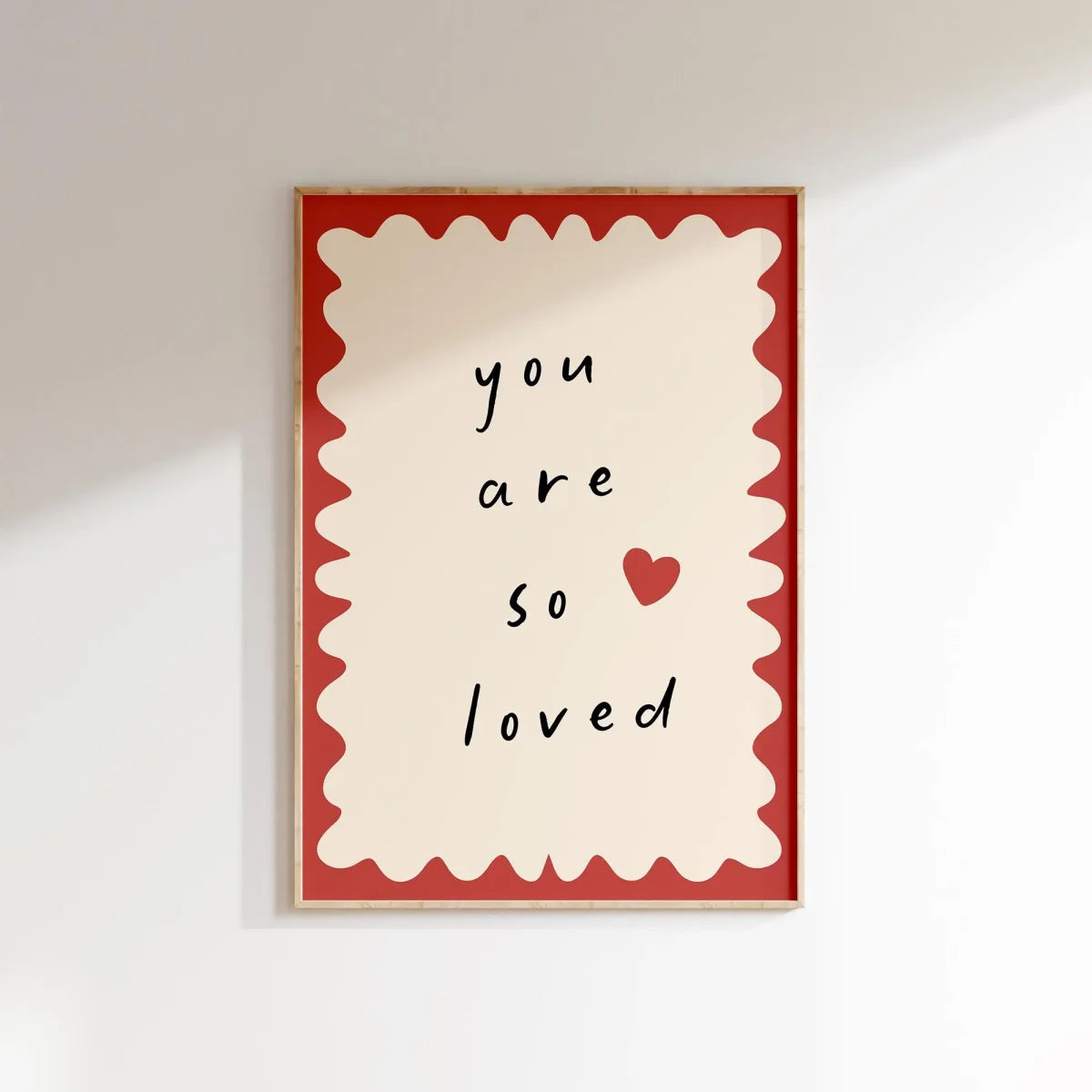 Framed artwork with 'you are so loved' text and a heart on a white wall.