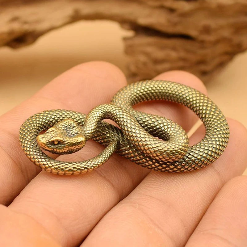 Gold snake-shaped pendant held in a hand with a wooden background