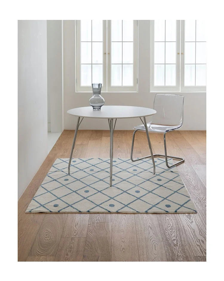 Round table with a clear chair on a patterned rug in a room with large windows.