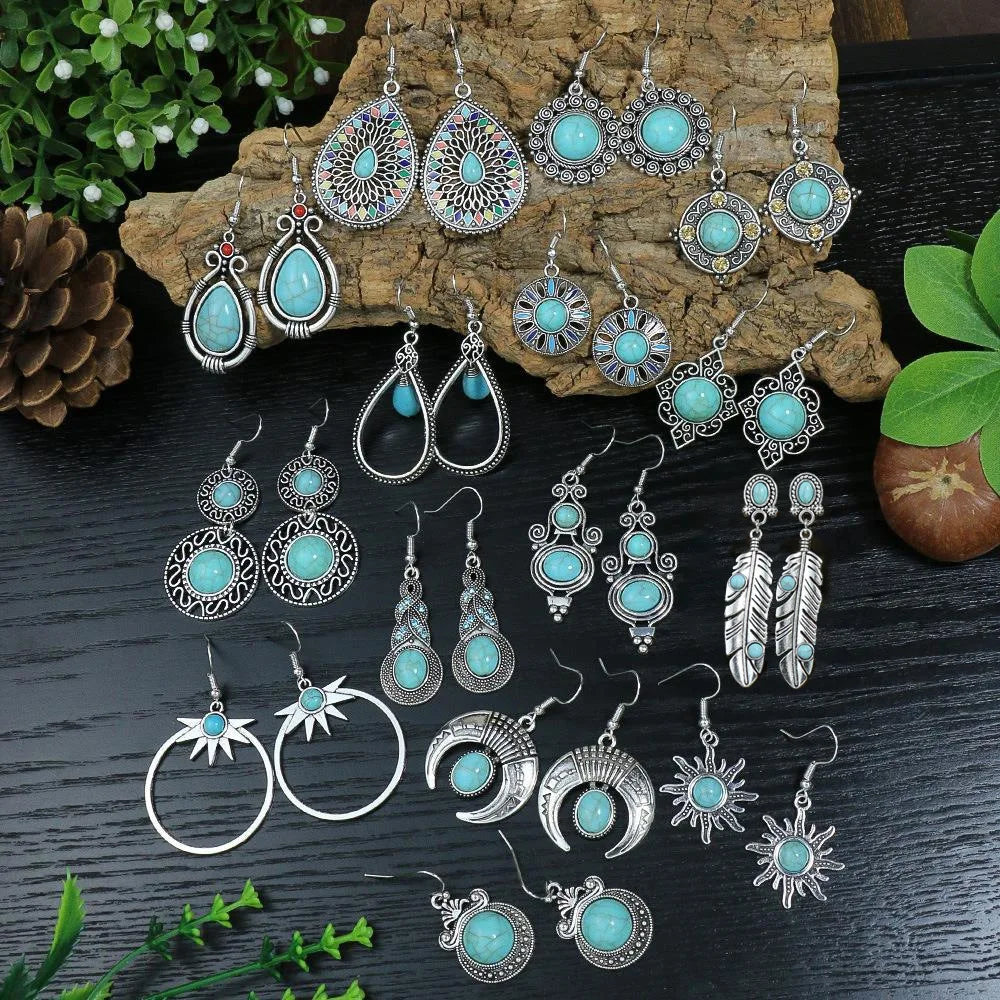 Collection of turquoise and silver earrings on a wooden and dark surface with greenery.
