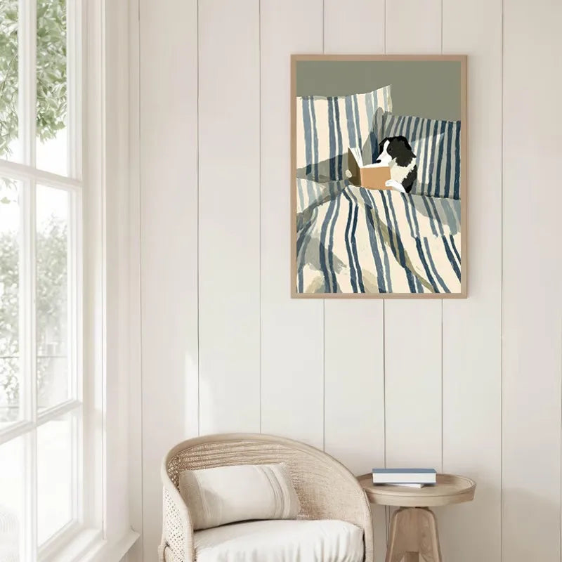 Framed artwork of a dog reading a book on a striped couch in a room with a window and chair.