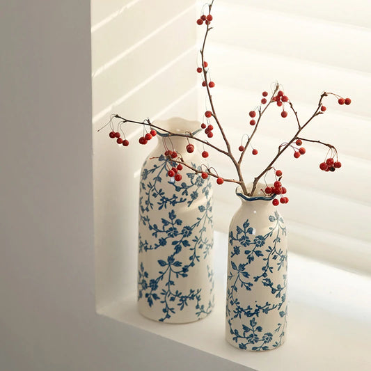 Two decorative vases with blue floral patterns holding branches with red berries on a white background.