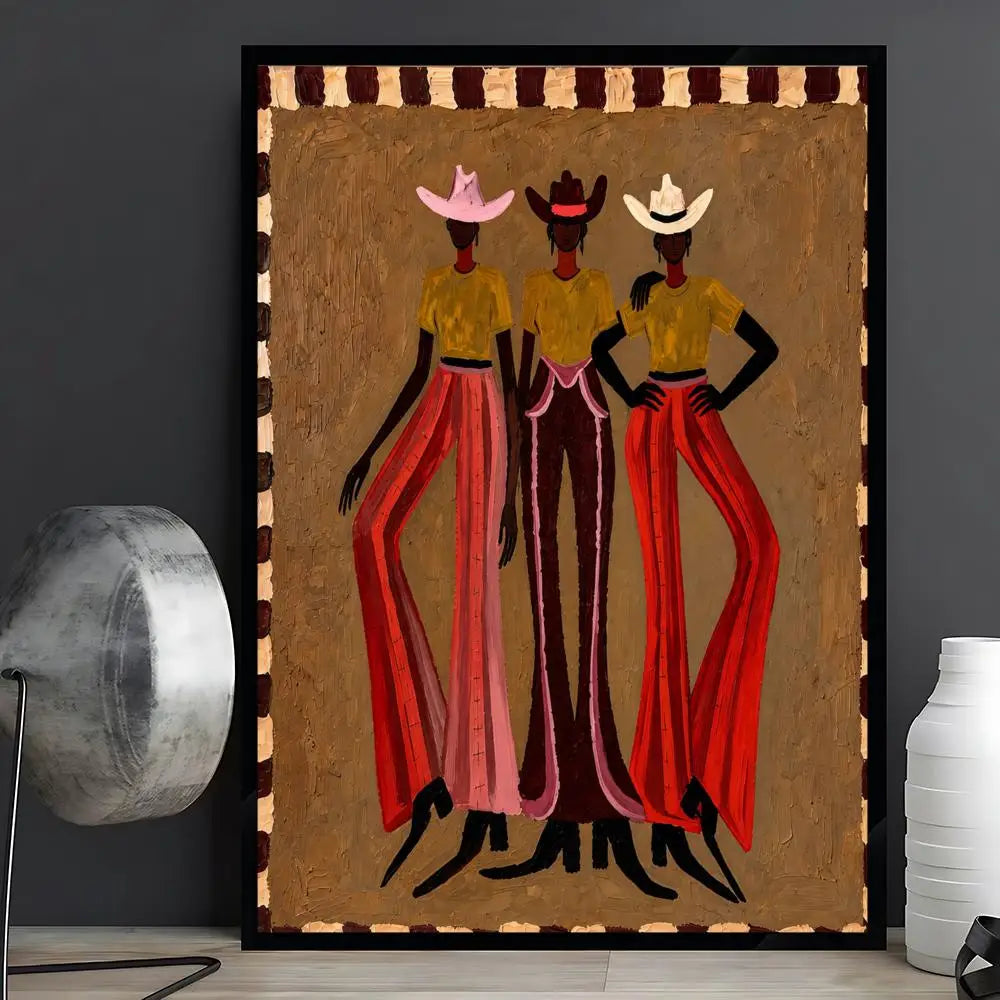 A framed art print featuring three stylized Black women in cowboy hats and long red and pink skirts, displayed on a shelf next to a silver lamp and a white vase against a dark gray wall.