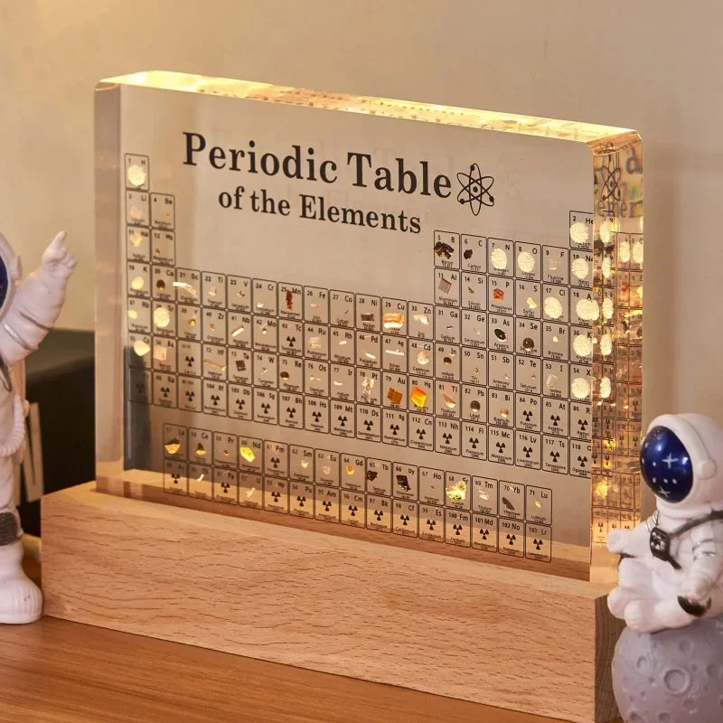 Luminous periodic table of elements display with wooden base and decorative figures.